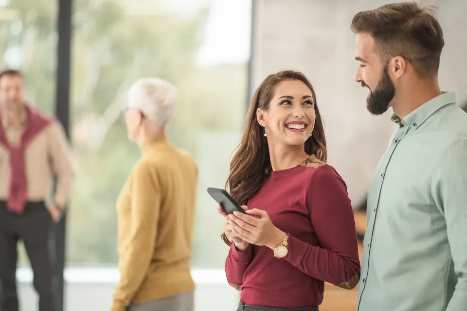 Colleagues talking in a bright office, one holding a phone