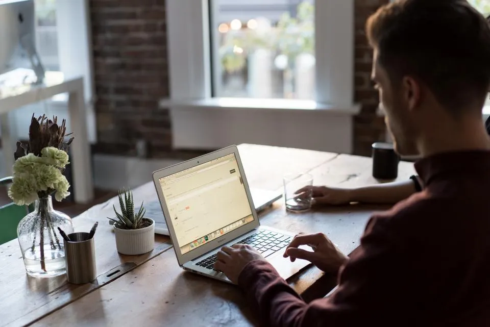 A person concentrating on work at a laptop at a wooden desk