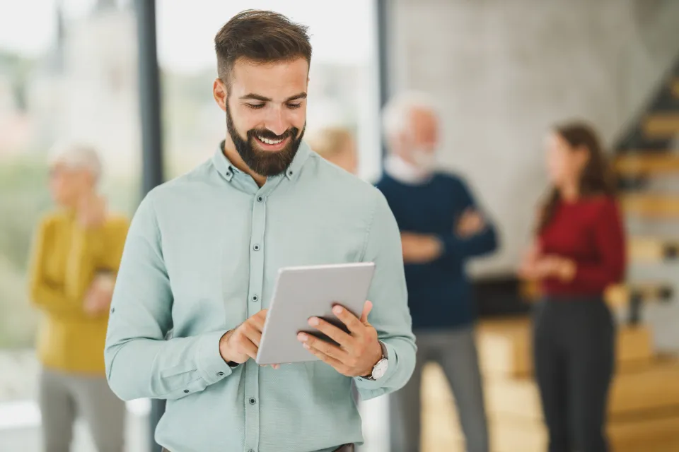 A man reviewing work on a tablet in a busy, bright office