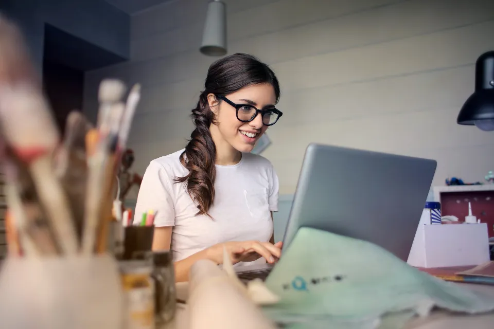 A woman smiling while working on a laptop in a creative studio