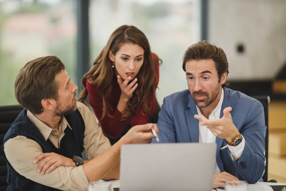 Three colleagues working through a problem together around a laptop