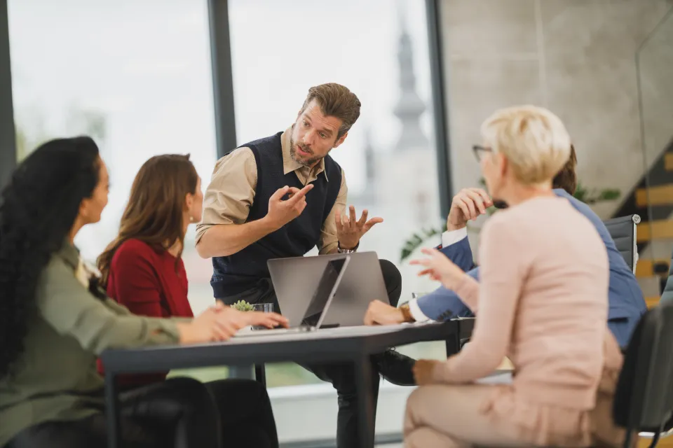 A small team in discussion around a table with laptops in a bright office